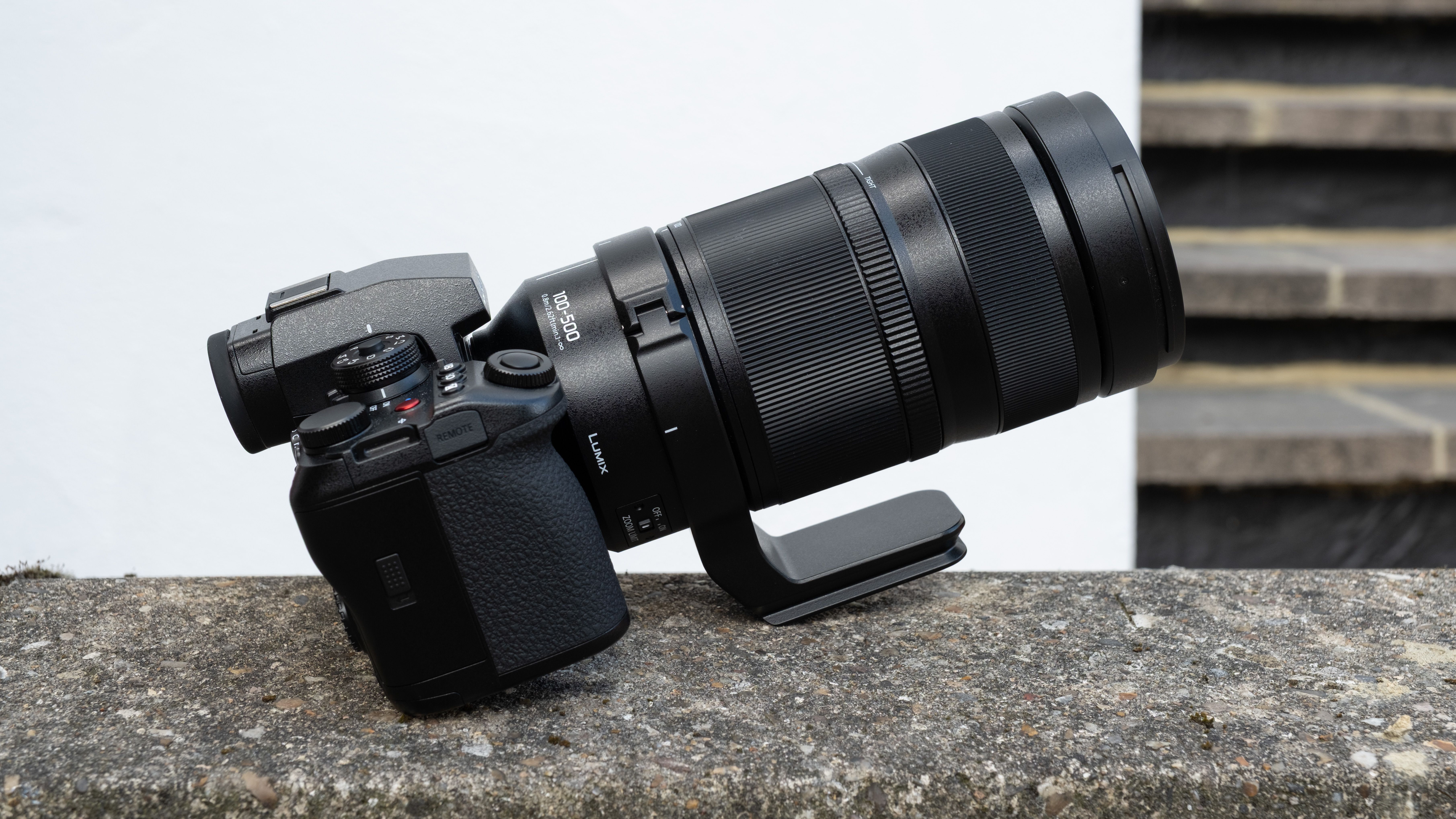 Panasonic Lumix S1II camera with a Lumix S 100-500mm f/5-7.1 lens attached, balanced on a wall