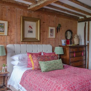 bedroom in Tudor house with wooden panelled wall, beamed ceiling and colourful bed throws