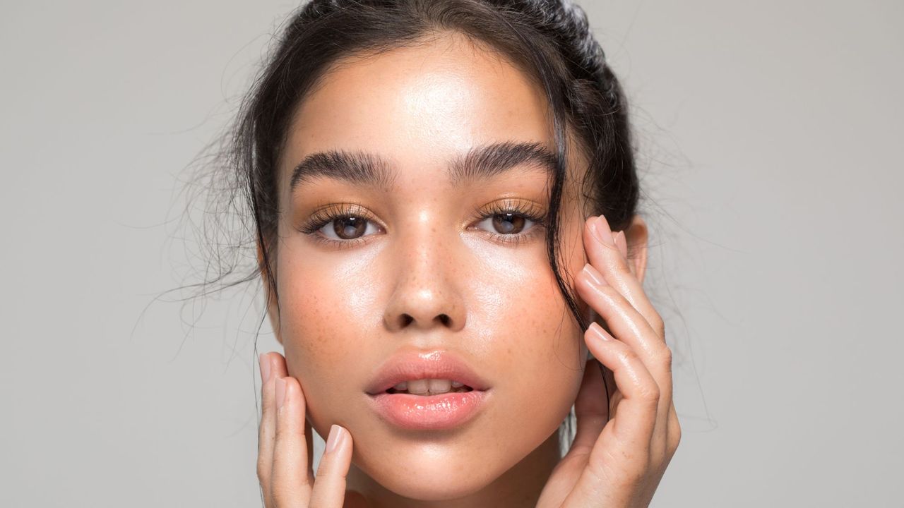 A close up of a woman with beautiful glowy, clear and even skin with her face in her hands