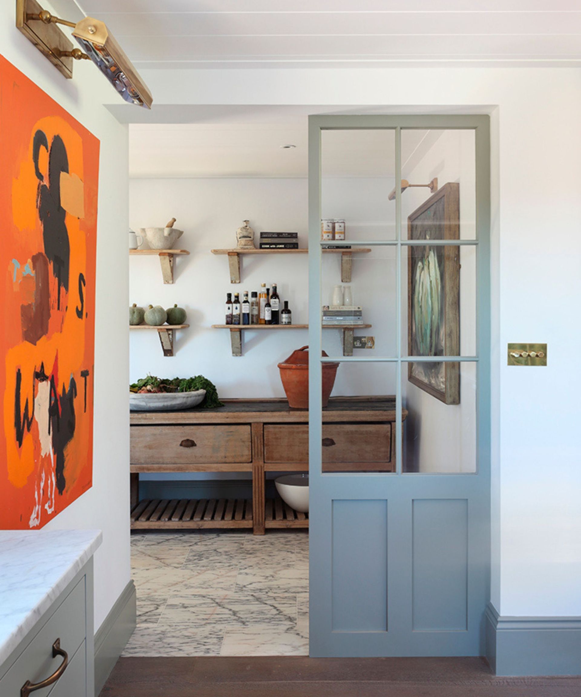 The doorway leading to a rustic style kitchen. The doors has a panel of glass and the woodwork is painted in a gray color, imbued with a slight blue tinge.