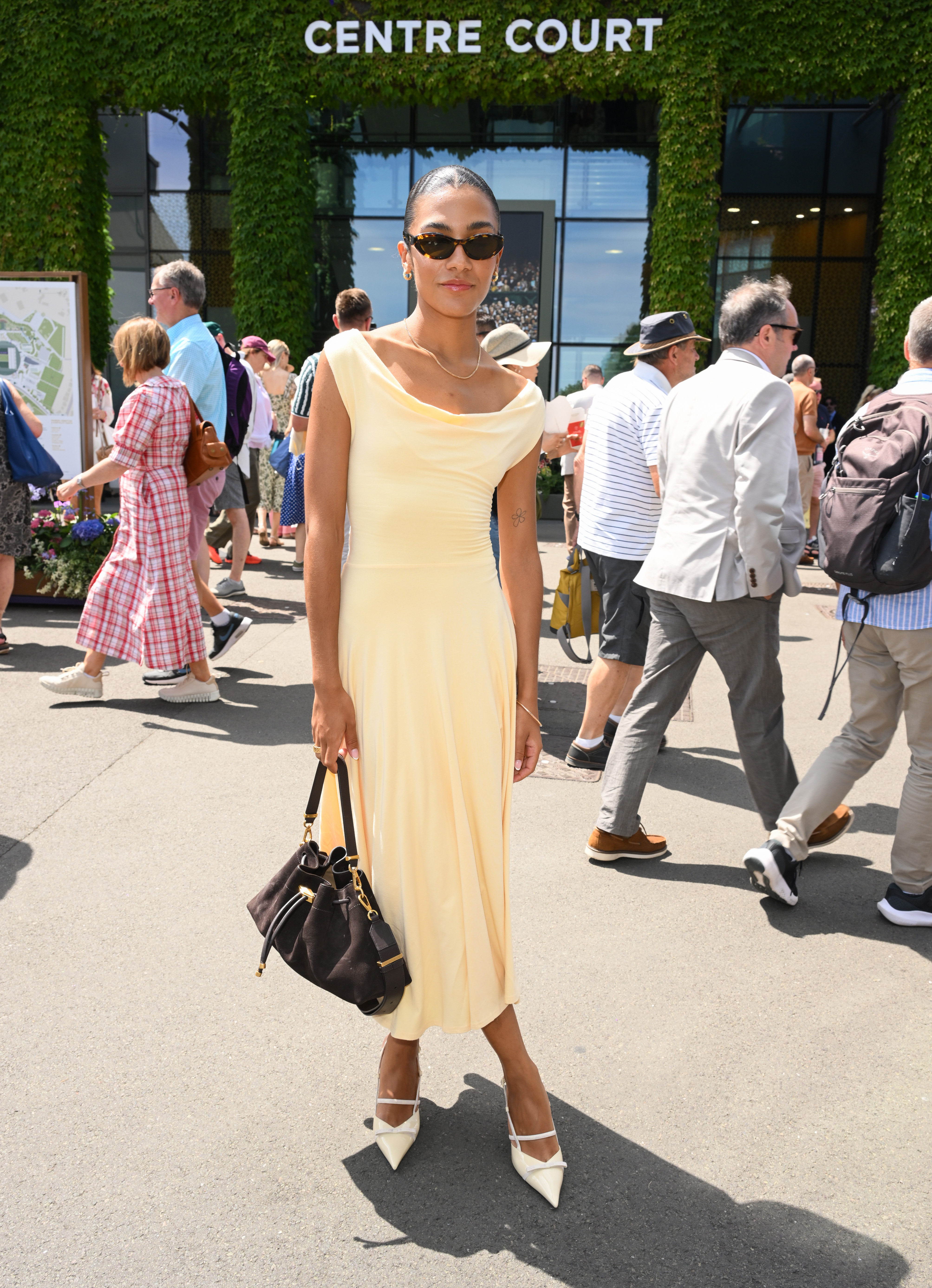 Olivia Dean wears a butter yellow dress and cream heels with a brown suede bag to Wimbledon.