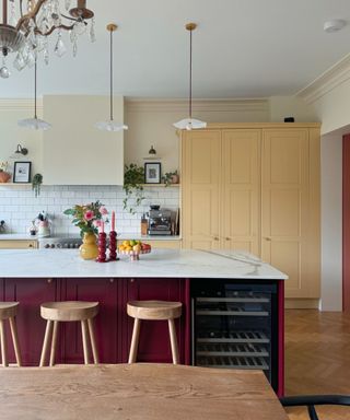 A kitchen with off-white walls, white subway tiles, yellow cabinets and a burgundy kitchen island