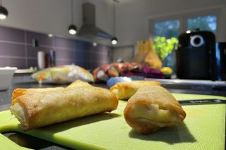Airfryer with spring rolls in front on kitchen table