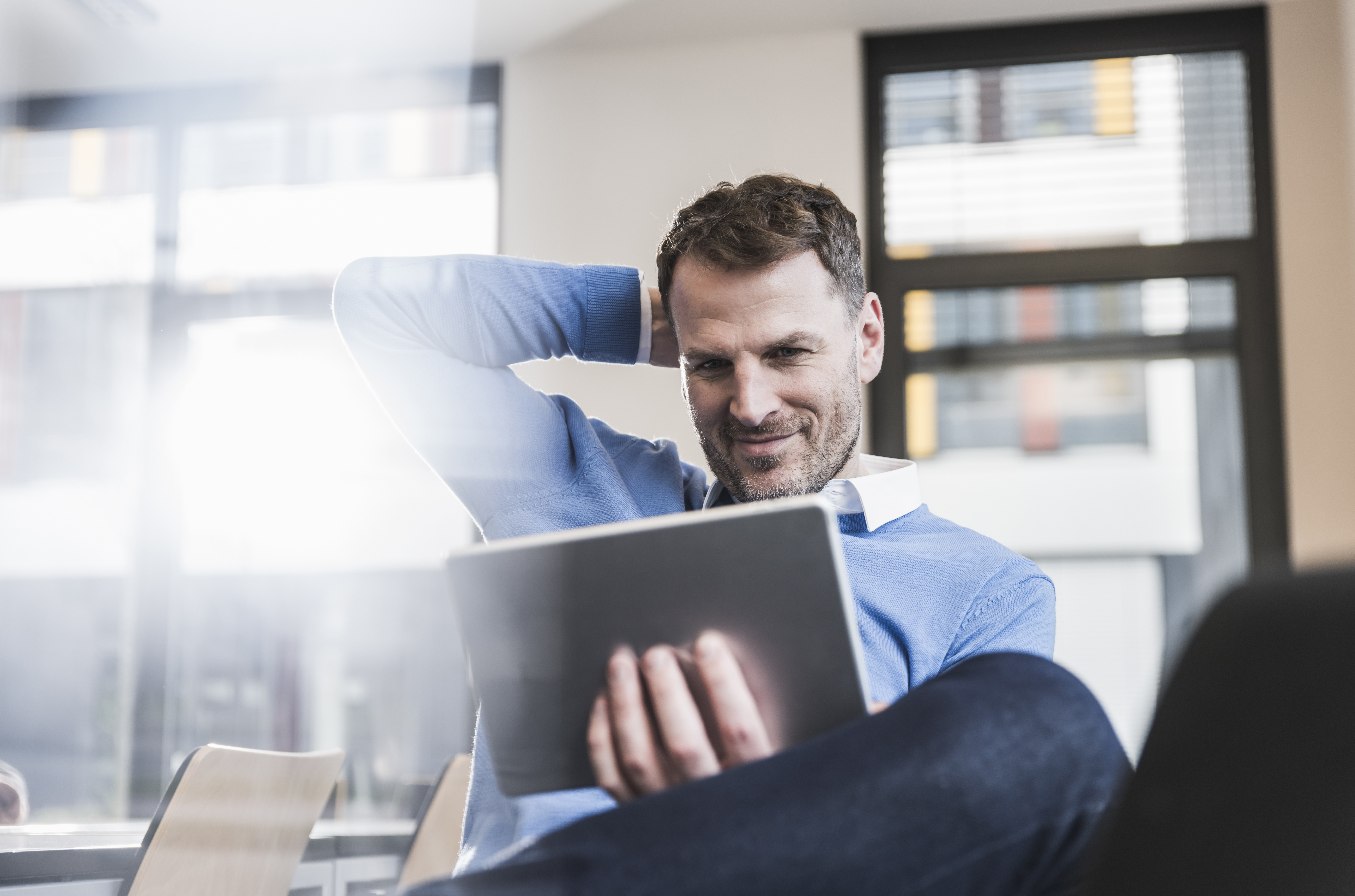 A fortysomething man sits at his desk in his office using his tablet.