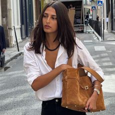 A woman walking down the street wearing a classic white shirt carrying a chic suede handbag