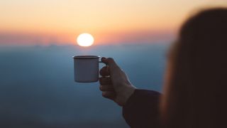 A person holding a cup of coffee with the sunset in the background