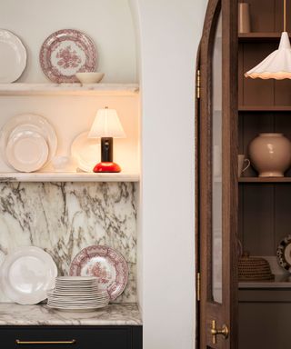 arched shelving in a traditional kitchen with marble countertops vintage crockery and an unexpected red lamp