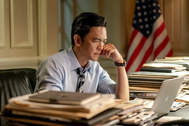 John Cho wears a blue shirt and tie and sits at a desk full of papers in &#039;Tempest.&#039;