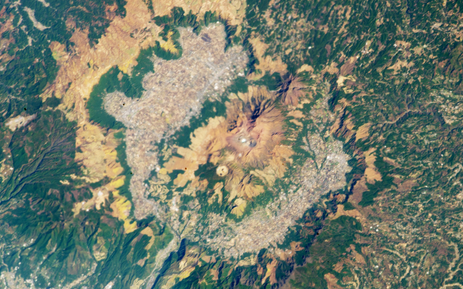 A satellite photo showing a large caldera with a cluster of volcanoes in its center and a ring of urban and agricultural land