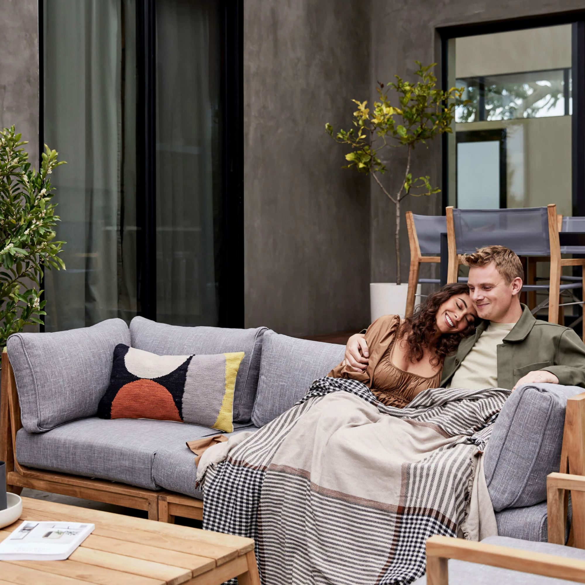 A couple relaxing on the Teak Outdoor Sofa with Armless Chairs - 5 Seat.