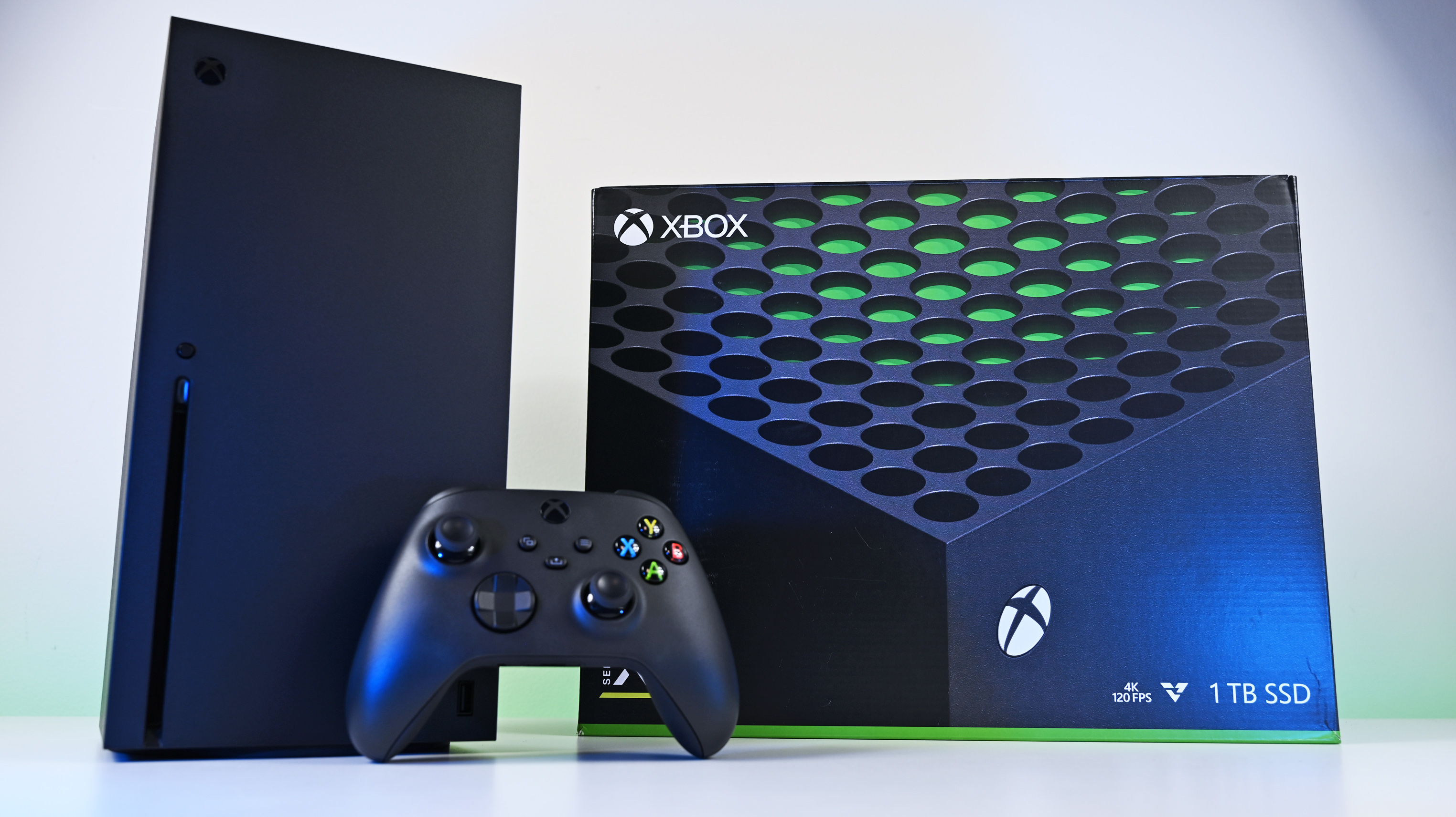 Front view of an Xbox Series X console and wireless controller next to the official retail packaging box under clean, bright studio lighting.