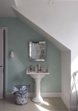 green toned bathroom wallpaper with white intrictae pattern running through, sloper roof and distressed mirror