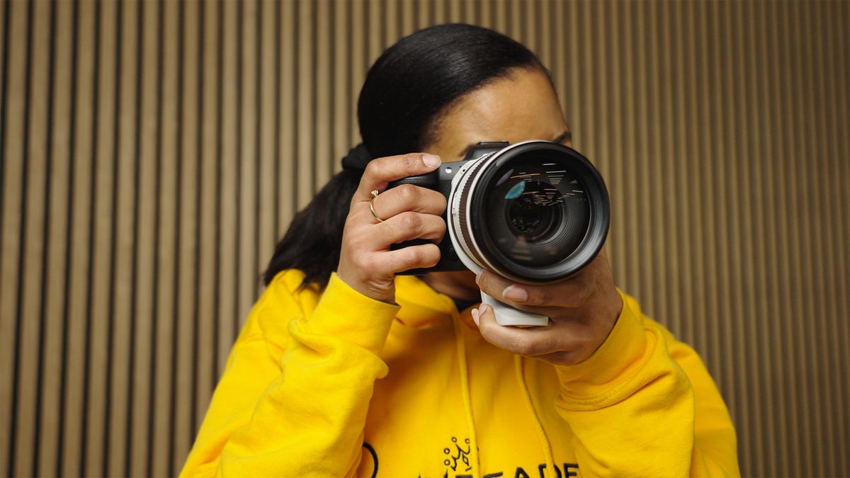 Woman holding a camera with the lens pointed towards the screen