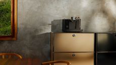 A black Fellow Series 1 espresso machine on a tan, metal cabinet of drawers in front of a gray limewash wall.