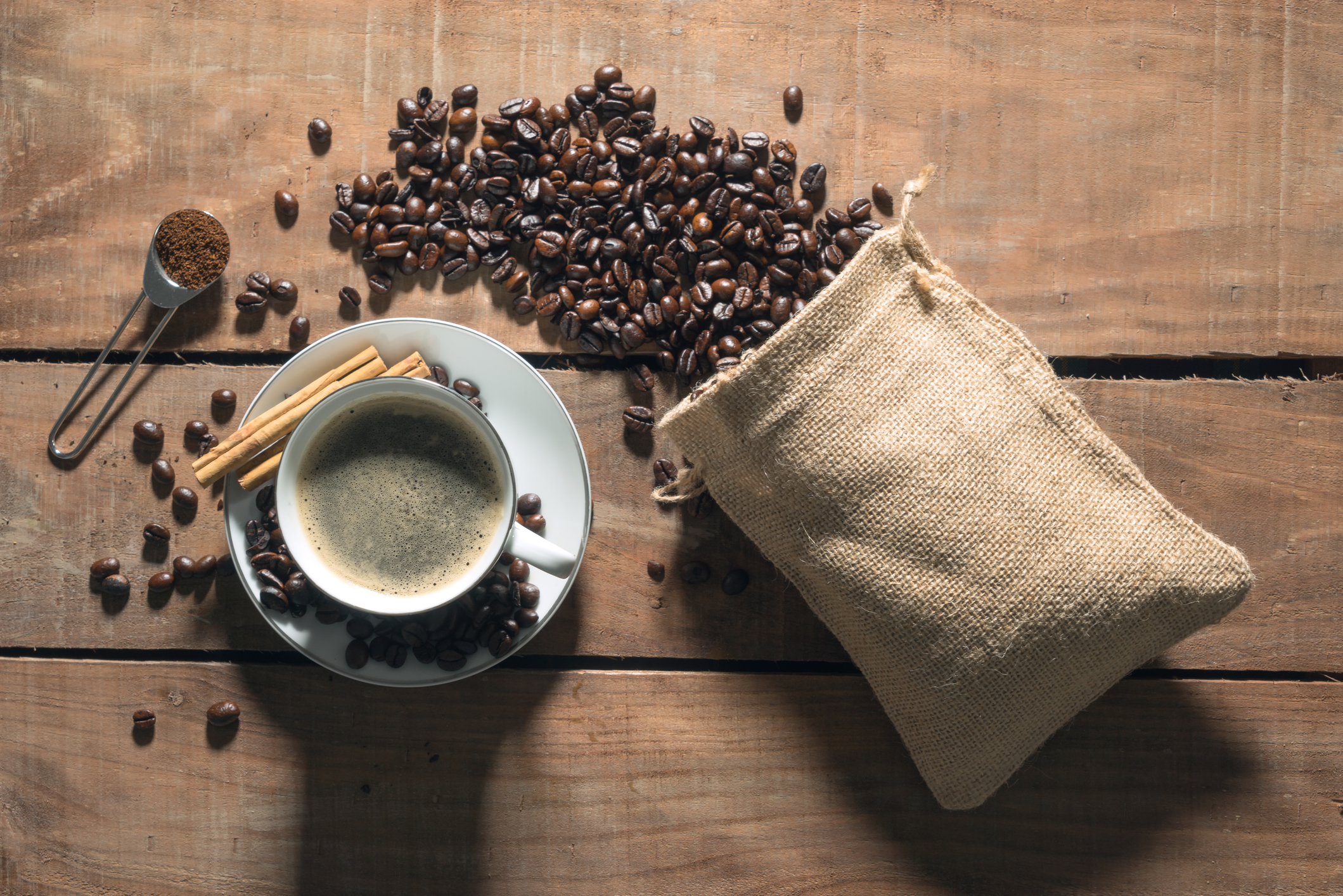 a burlap bag brimming with coffee beans next to a cup of coffee on a saucer