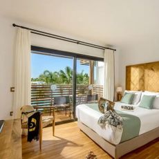 A modern bedroom with a pool view, sunhat and sunbag on a chair.