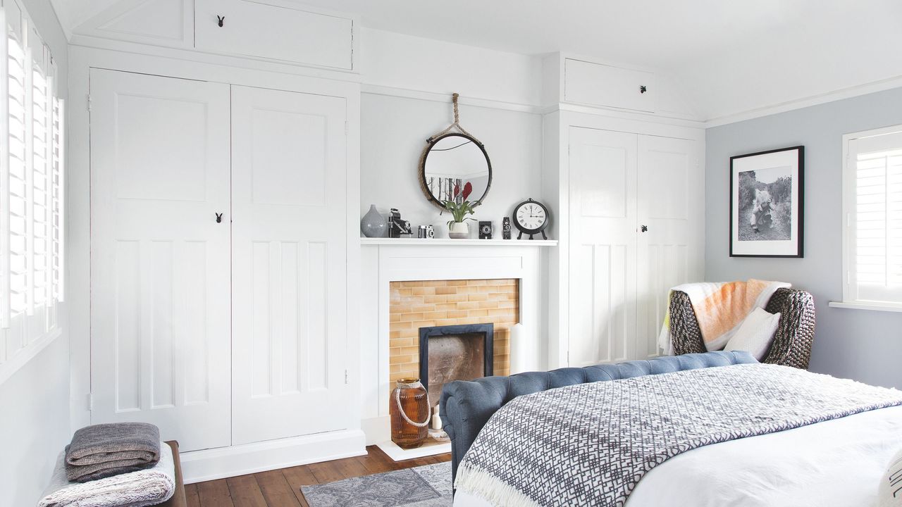 Bedroom with white fitted wardrobes, a fireplace in the middle of the room, and a white bedspread with blue bed frame