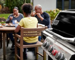 Weber Genesis 335 gas grill on a patio with people in the background eating