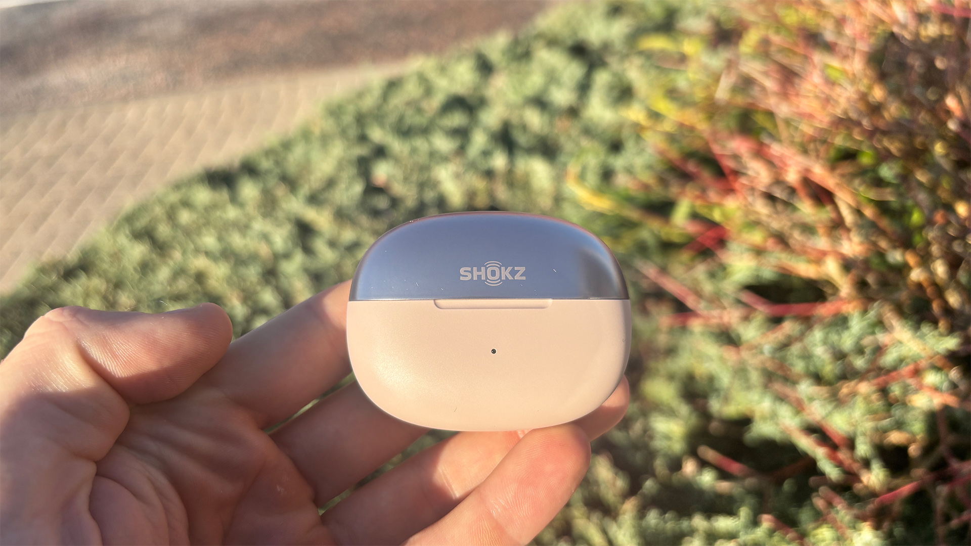 Shokz OpenDots One open earbuds in closed case held in hand in sunny garden