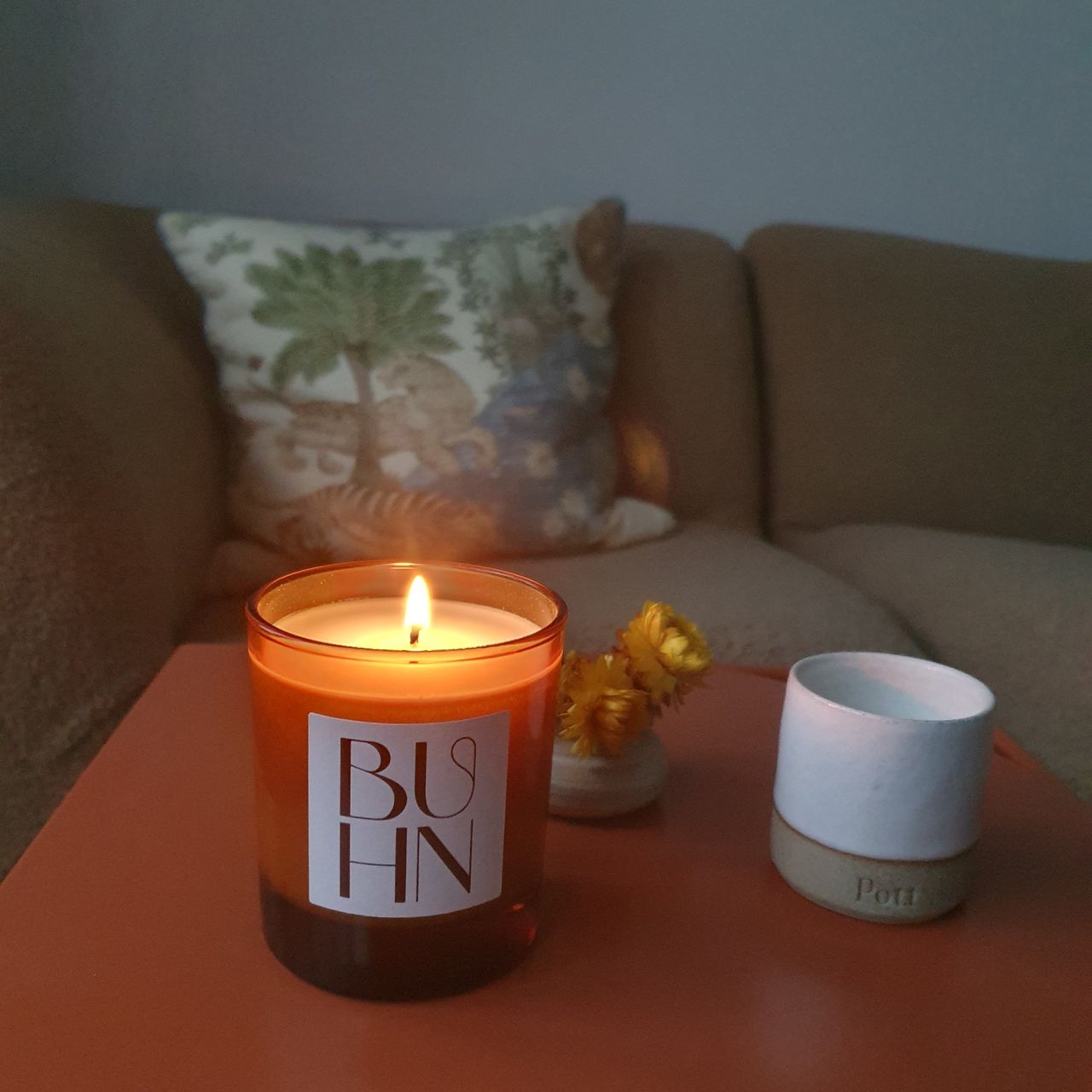 A lit Buhn scented candle next to a mini Pott candle on an orange coffee table