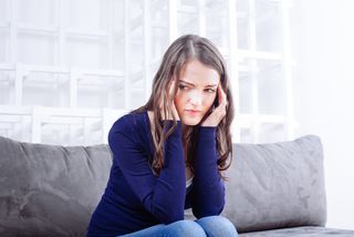 A woman sits on a couch, looking upset.