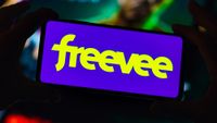 A phone with the 'freevee' logo is held by two hands in the dark.