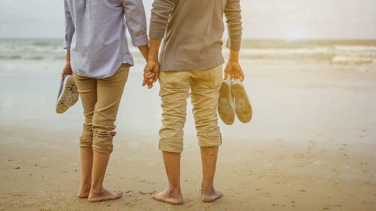 A couple standing on a beach holding hands, seen from the shoulders down