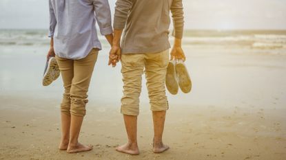 A couple standing on a beach holding hands, seen from the shoulders down