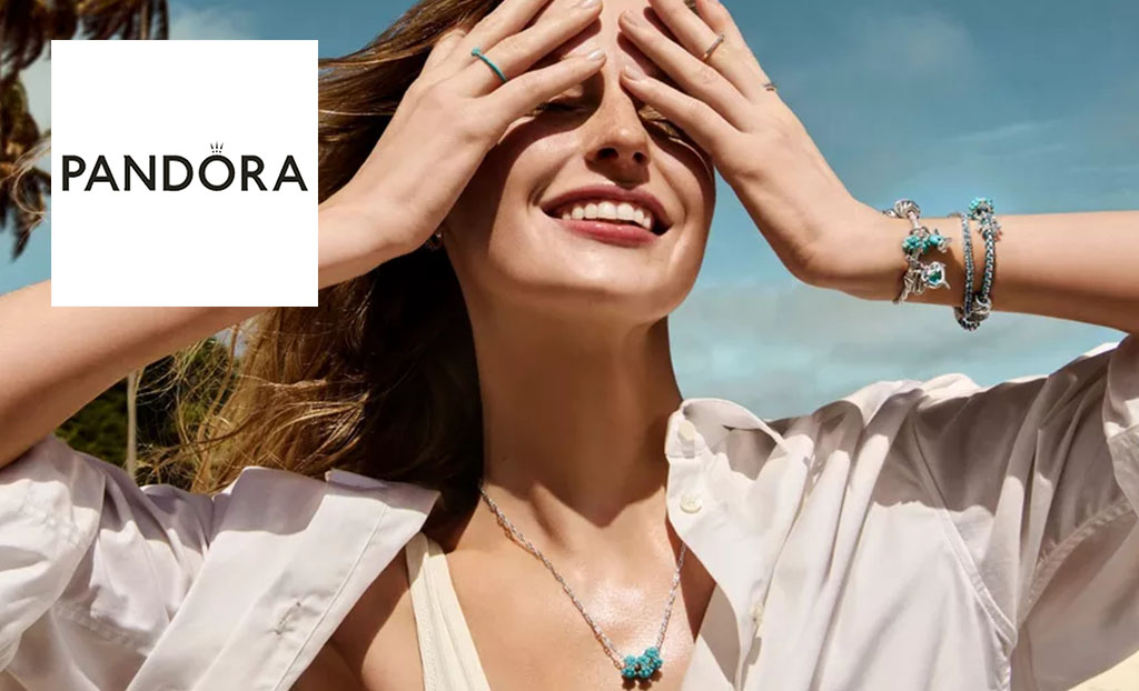Woman on beach wearing shirt shirt and jewellery. Pandora logo in top left corner
