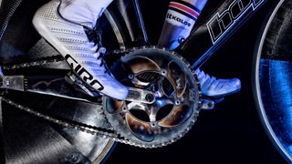 A close up of a mirror polished 5 arm crankset, propelled by a white Giro shoe