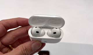 En hand håller upp ett par Apple AirPods Pro 2 som ligger i sitt öppna fodral.