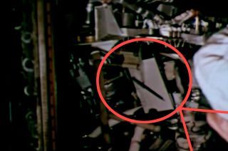 Still frame of the 'Friendship 7' cockpit with the scroll visible at the center of photo, in front of John Glenn.