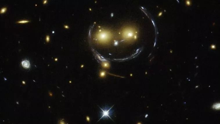 A telescope image of warped yellow starlight forming a smily face against a black background.