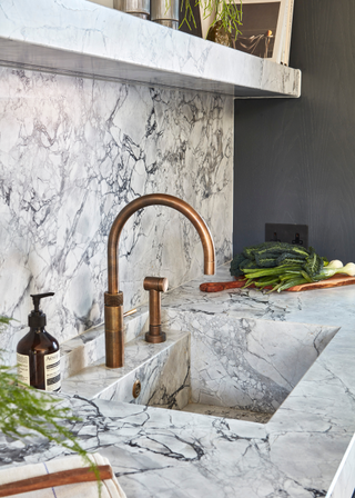 full marble clad sink with a leathered finish. sink has copper brassware