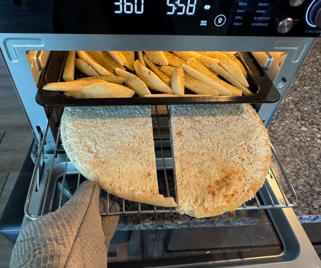 The Typhur Sync Air Fryer Oven on a granite work top, open, pulling a tray with flatbread out.