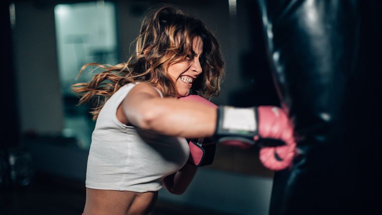 Strong young women with boxing gloves, punching a punching bag in gym alone