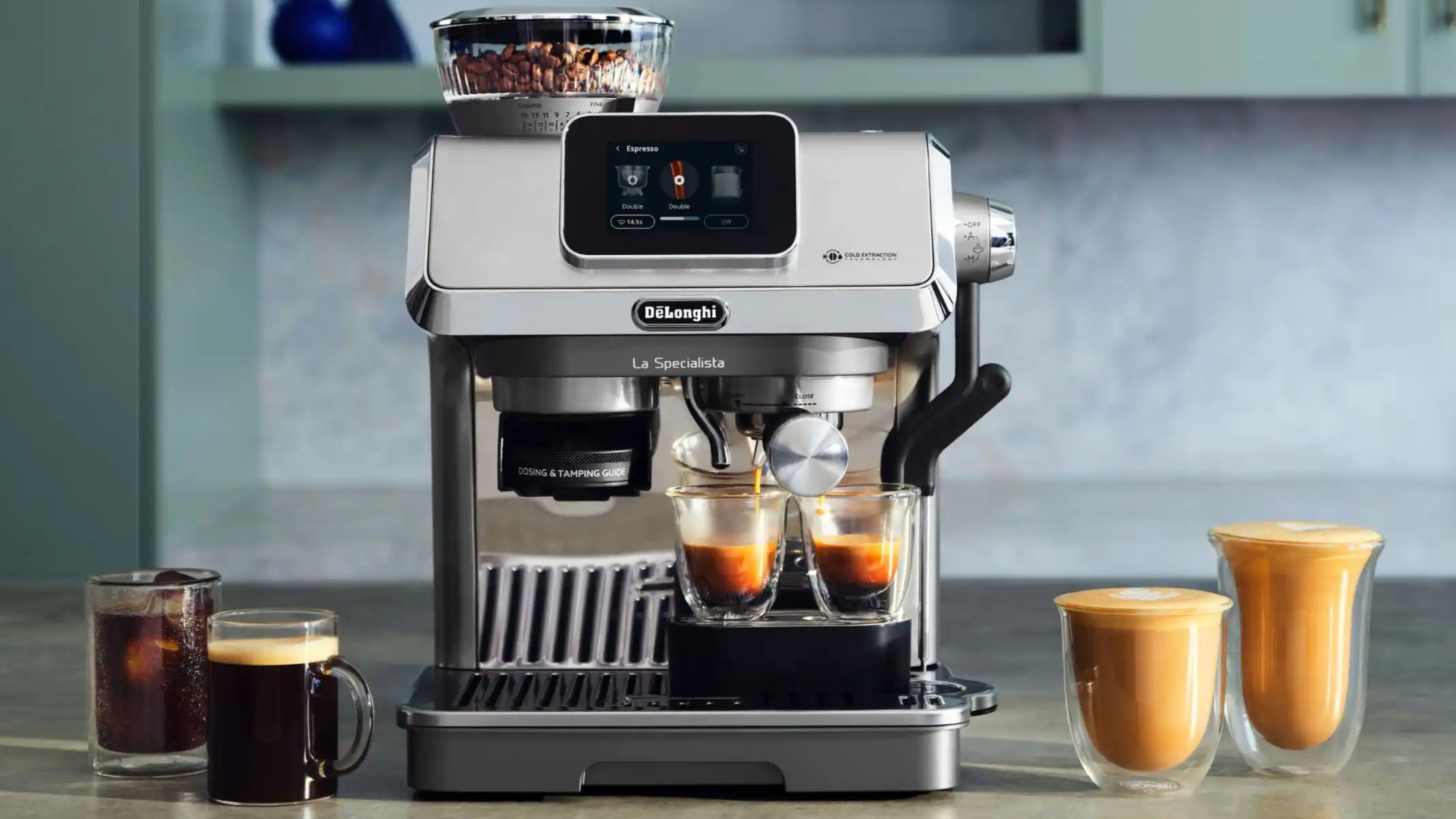 Image of the De&#039;Longhi Specialista Touch espresso machine in silver sitting on a gray kitchen counter in a teal kitchen. There are two espresso shots being brewed and mulitple coffees sitting on the counter beside the machine