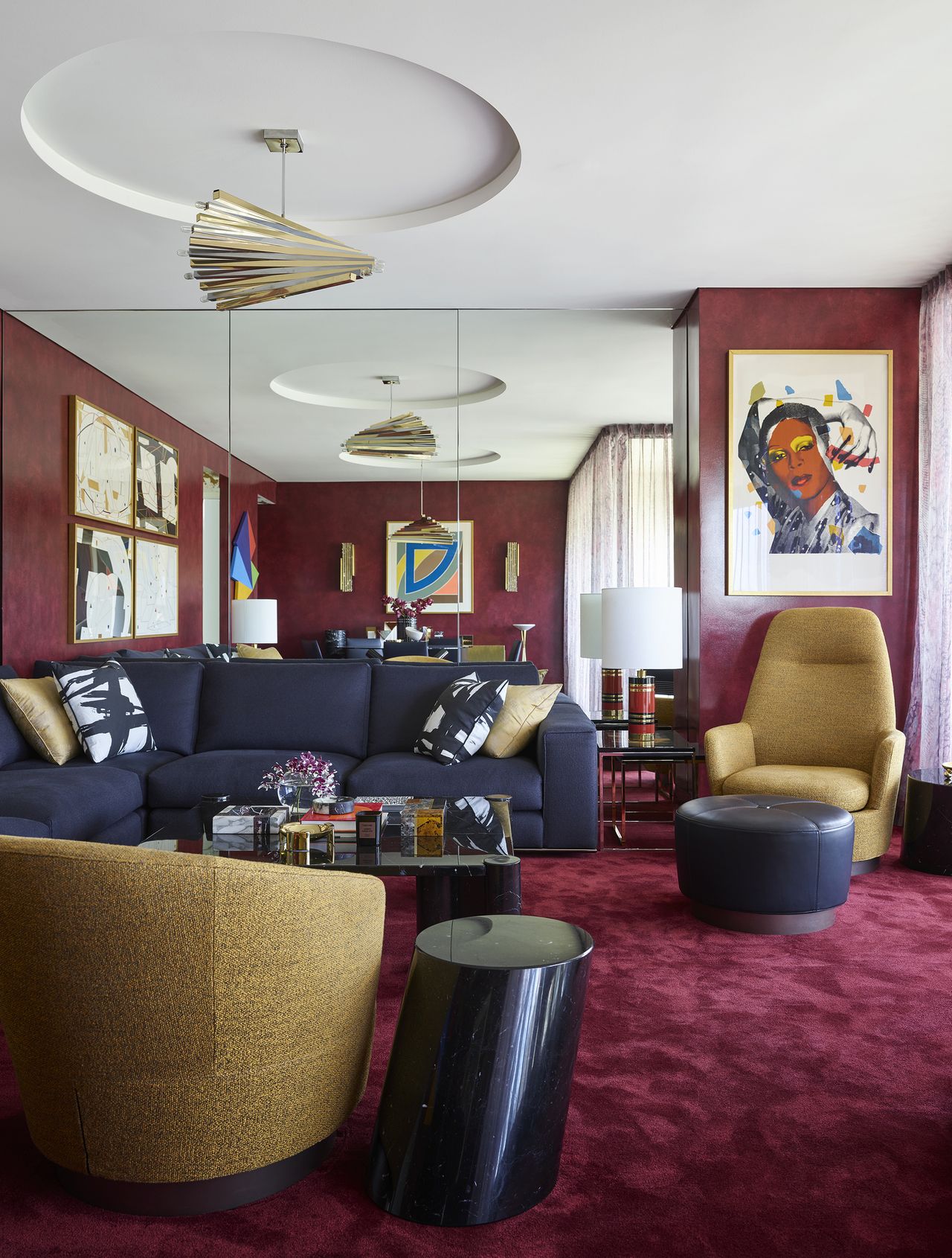 maximalist living room with wine colored carpets, mirrored wall, navy sofa, mustard yellow armchairs, artwork, and coffee table with lots of decor