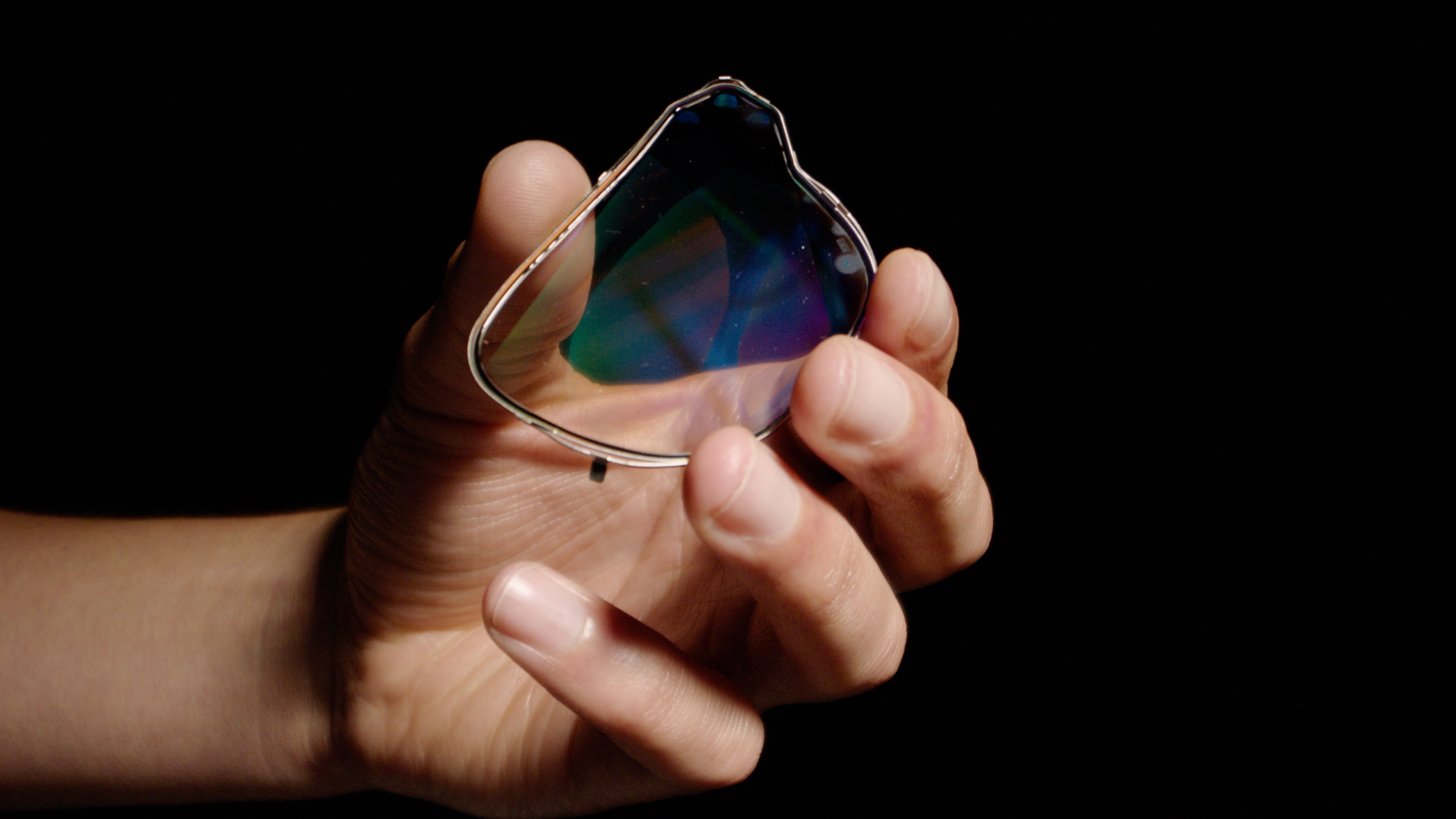 A silicon-carbide waveguide held in someone's hand in front of a black backdrop