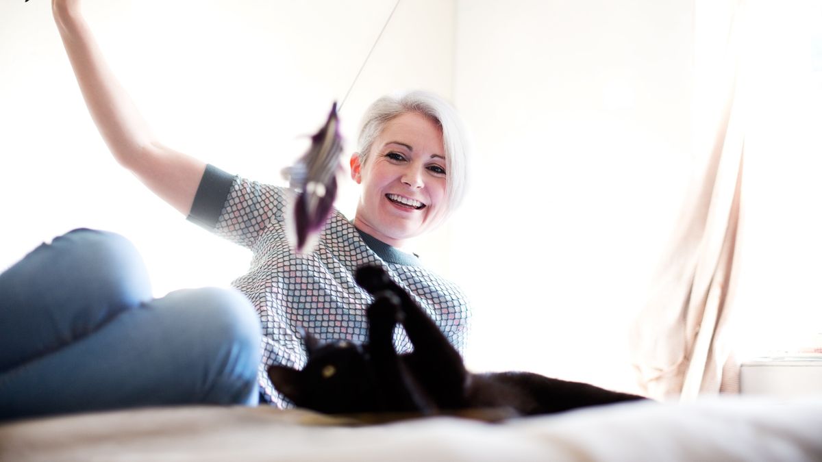 Woman playing with her cat using a wand toy