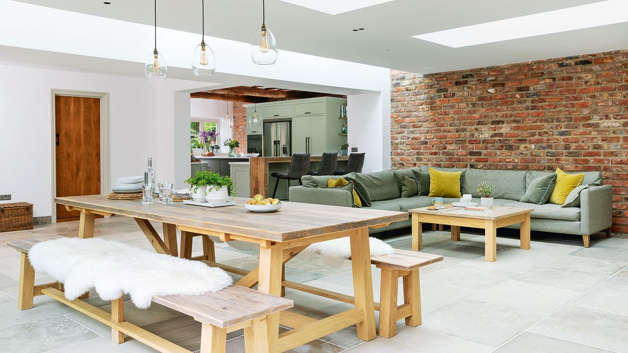 Modern country open plan living room with farmhouse style dining table and exposed brick wall at back of room