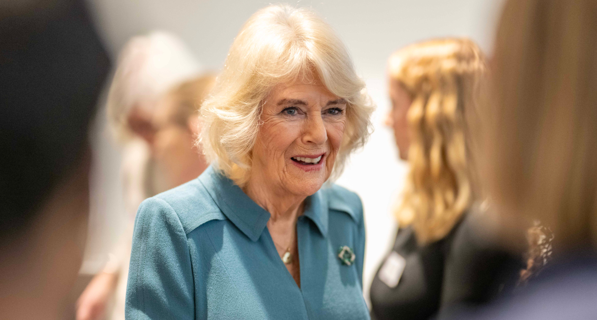 Queen Camilla smiling in a group of people, wearing a blue dress
