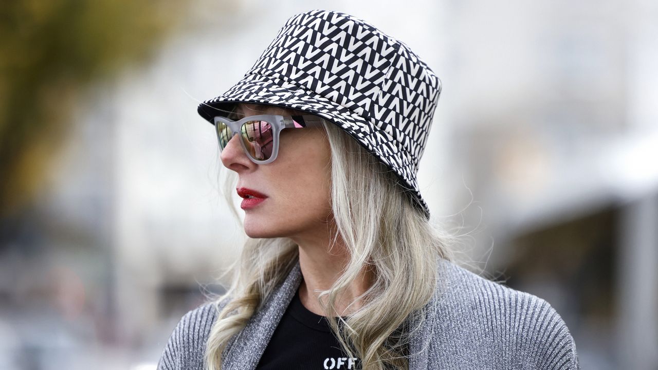 Best lipsticks for older women - Petra van Bremen wearing a black and white bucket hat by Valentino, a black t-shirt by Off-White, black shorts with belt by Off-White, a long silver knitted coat by Balenciaga, transparent frame sunglasses by Westward Leaning, - gettyimages1355367186