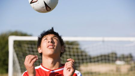 A boy wearing a red and white shirt looks up as a soccer ball floats above his head