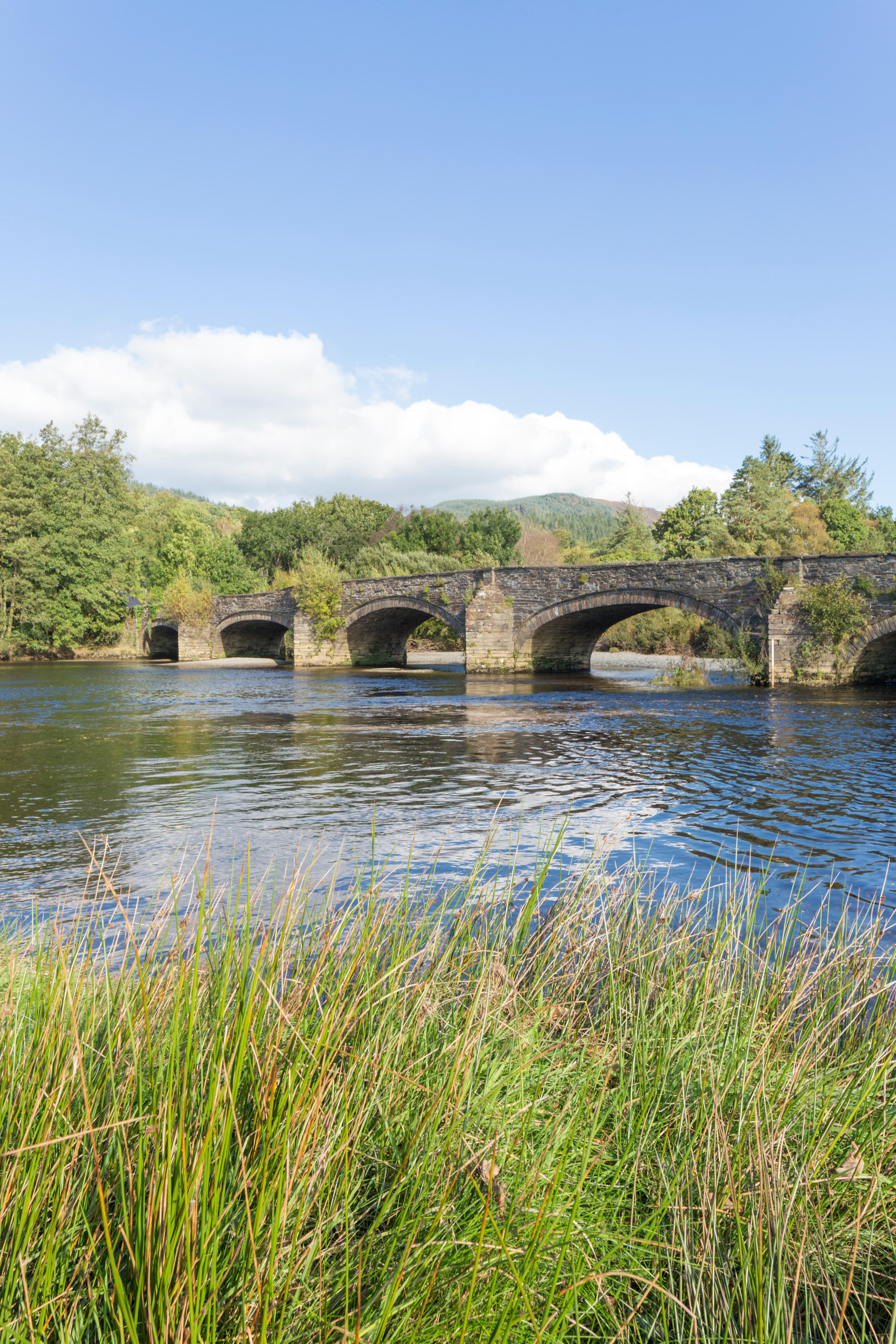 A historic grey stone, arched bridge crossing a wide river