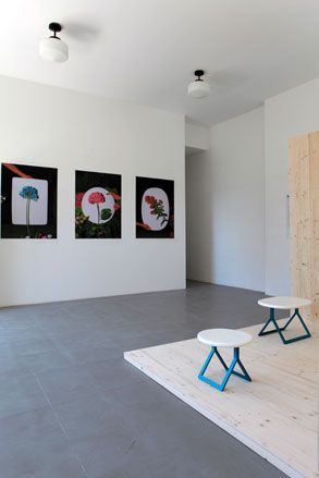 2 wooden circular chairs on a wooden platform in a room with wall art on white walls and grey floor