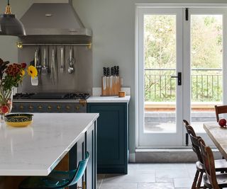 A kitchen layout with french doors looking out onto a terrace. There is a large metal extractor fan over a range cooker.