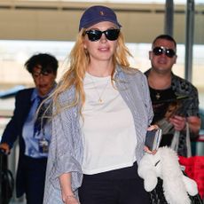 Lindsay Lohan walks through the airport wearing dark navy leggings with a white t-shirt and a striped shirt and white trainers.