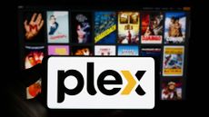 A phone with the Plex logo in front of an out-of-focus background of movie posters