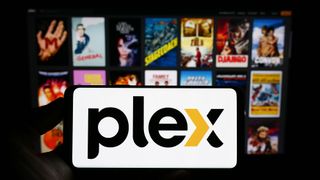 A phone with the Plex logo in front of an out-of-focus background of movie posters